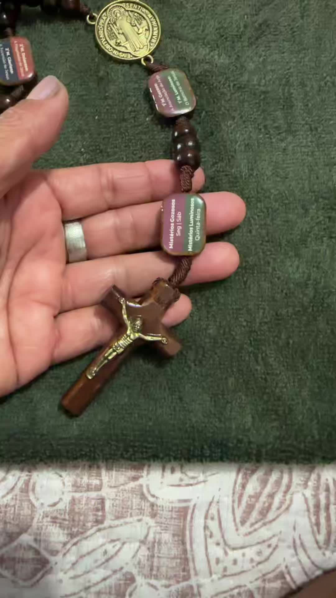 Cliente mostrando o crucifixo e placas dos mistérios sobre tecido verde